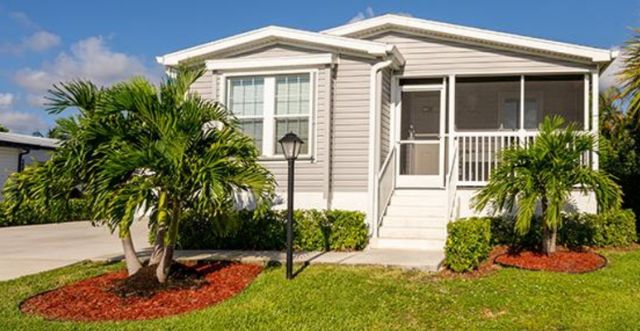 Manufactured home on lot, surrounded by grass and palm trees
